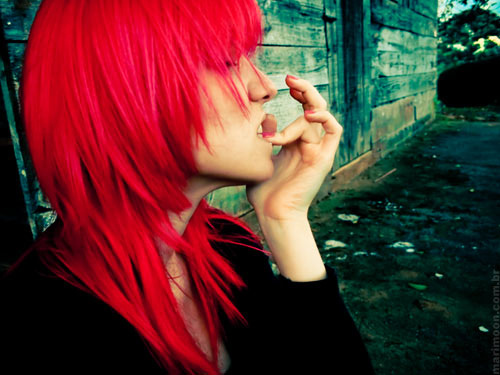 teenager with long red hair biting their nails in an allyway