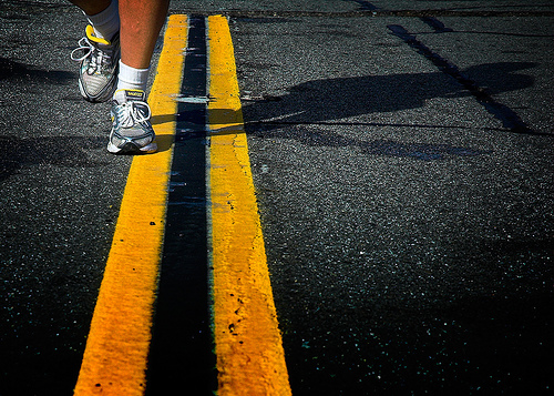 Legs with running shoes running on the highway where the double yellow solid lines are.